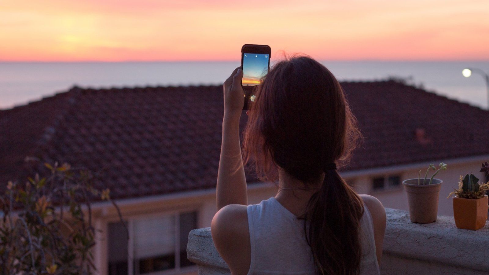 A female student takes a photo of sunset on her iPhone from her Flex apartment