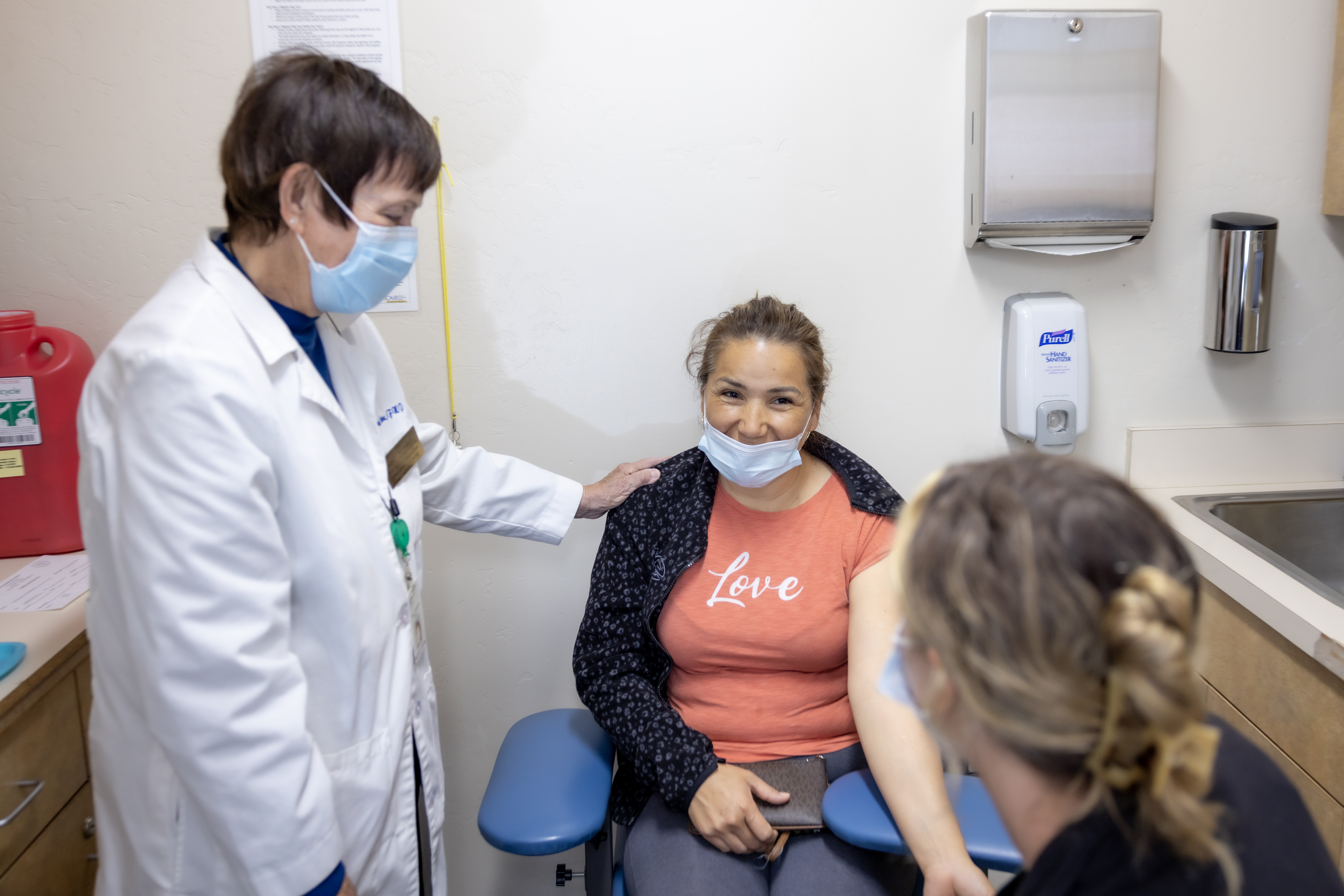 Two HPC nurses interact with a patient sitting in a chair wearing a mask