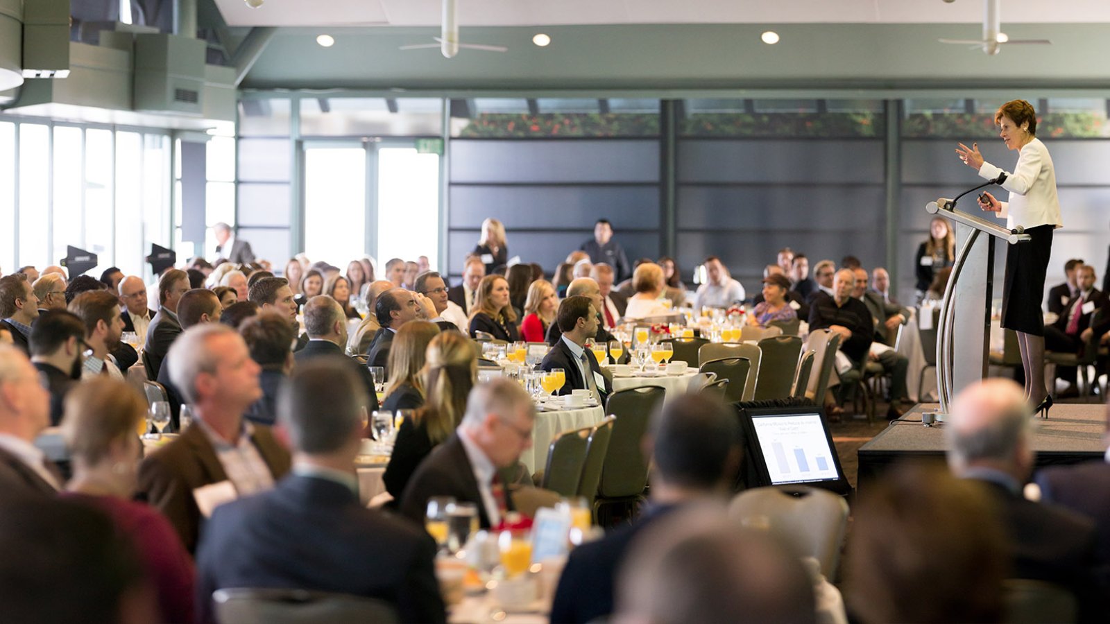 PLNU professor and chief economist, Dr. Lynn Reaser, addresses attendees from podium while they sit at round tables at the Economic Outlook Forum.