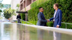 two men in suits shaking hands near a pond of water