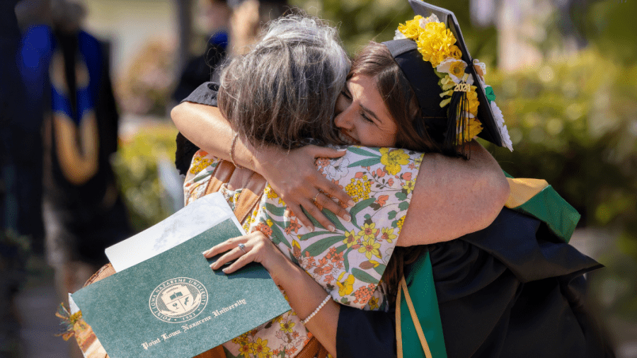 Graduating PLNU student hugging parent after receiving college diploma