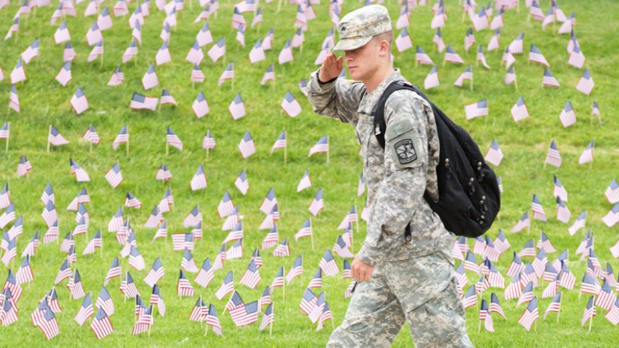 A military student salutes as he walks past a collection of american flags in the ground