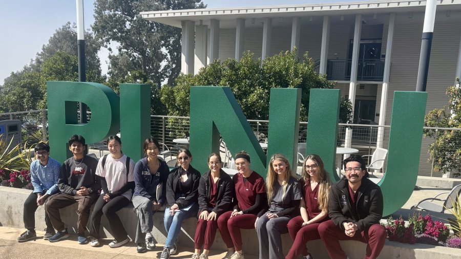 PLNU ALI outreach students pose in front university sign on Caf Lane.