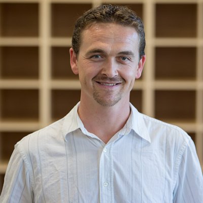 Brandon Sawyer headshot in front of a brown shelving unit