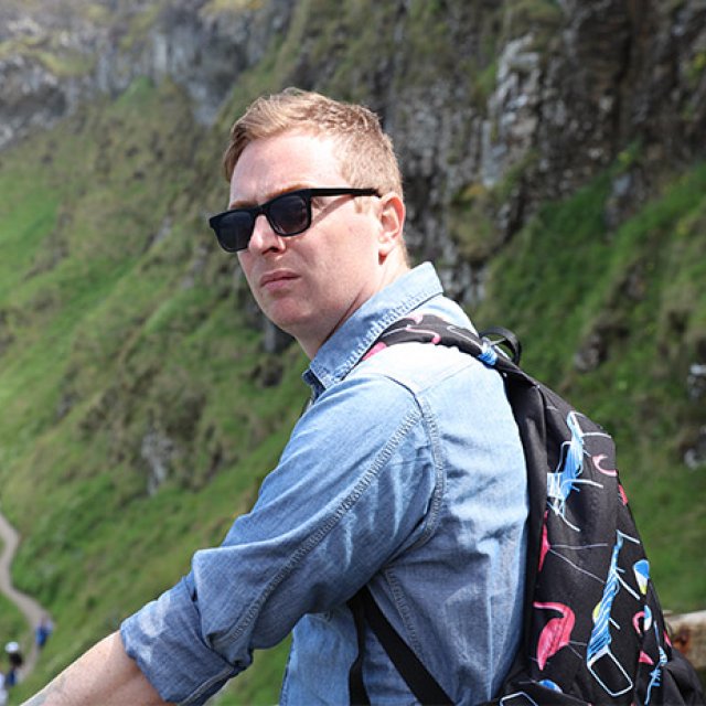 PLNU Alum Matt Applegate turns for a photo while hiking in a mountainous region.