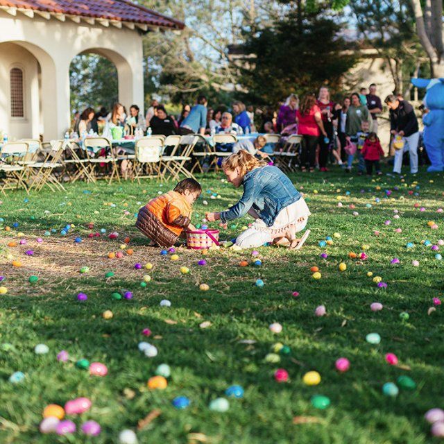 A PLNU student helps a child search for easter eggs on alumni lawn