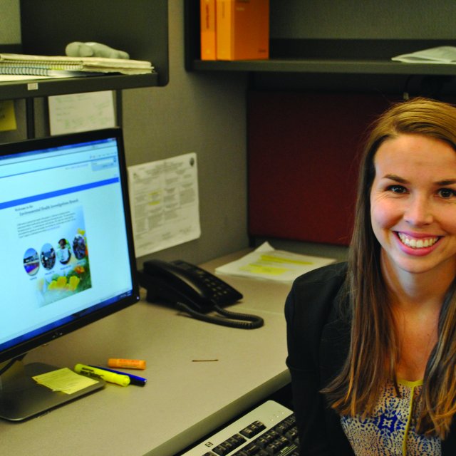 Lauren Nelson smiling next to her computer in her cubicle 