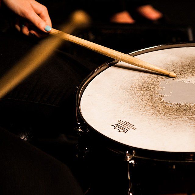 A pair of hands holding drumsticks hit a snare drum to a beat.