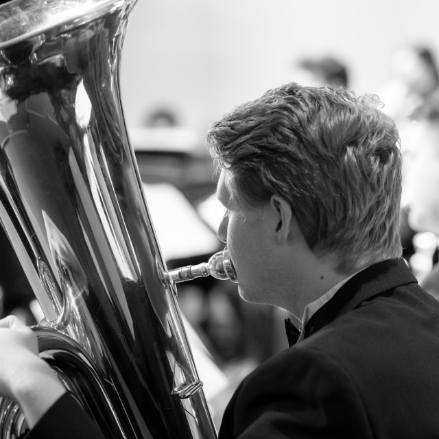 Male PLNU student in formal suit plays the tuba in a black and white photo.