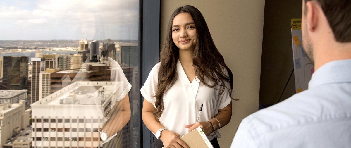 PLNU student posing for photo in downtown San Diego building with city in background.