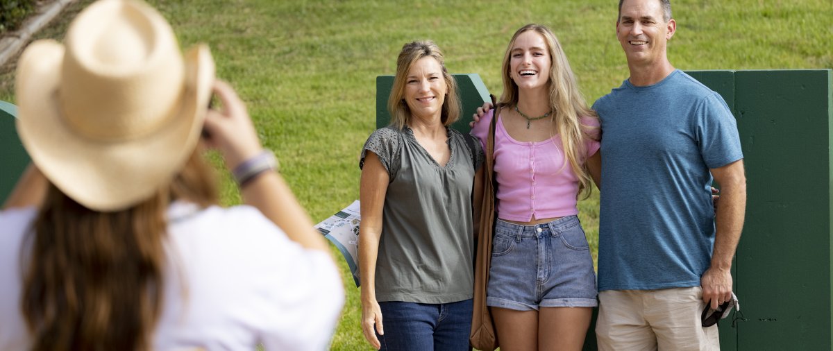 Woman taking photo of smiling PLNU student and parents
