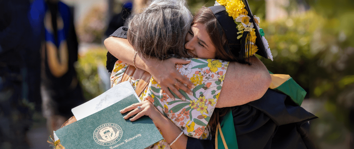 Graduating PLNU student hugging parent after receiving college diploma