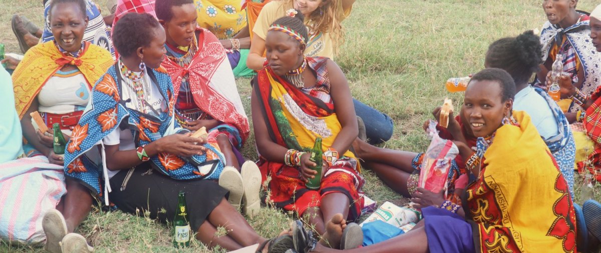 Emma McHugh and Kenyan women have lunch outside on the grass