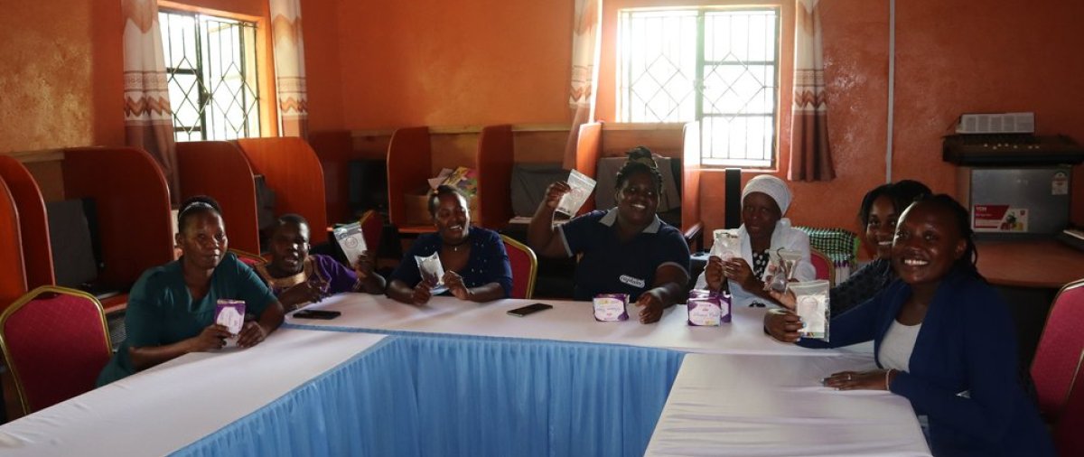 A group of Kenyan women sit around a table and hold up feminine products