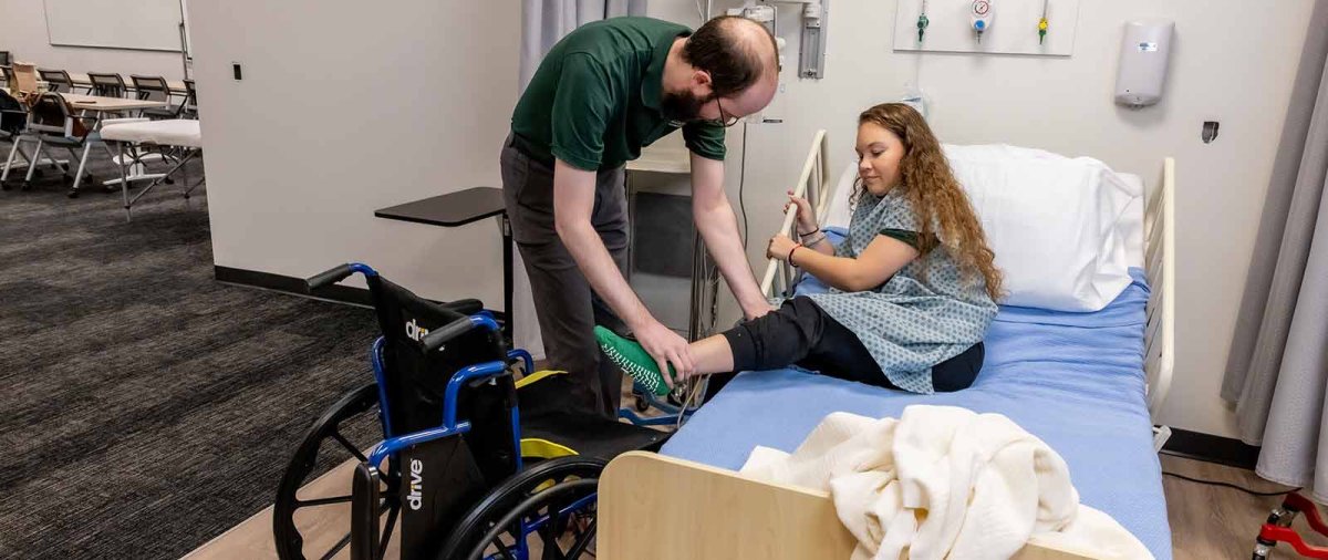 An MSOT student helps someone from a bed into a wheelchair