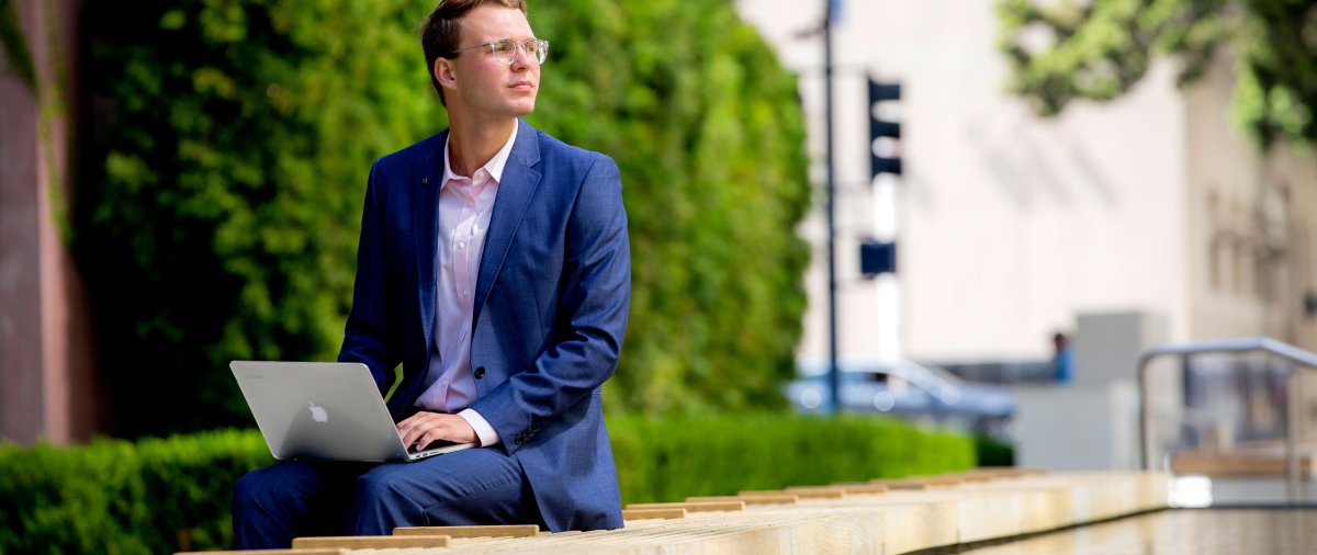 student sitting with laptop and gazing into the distance 