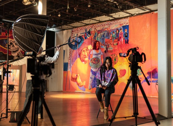 Alicia María Siu headshot, facing down in front of a mural