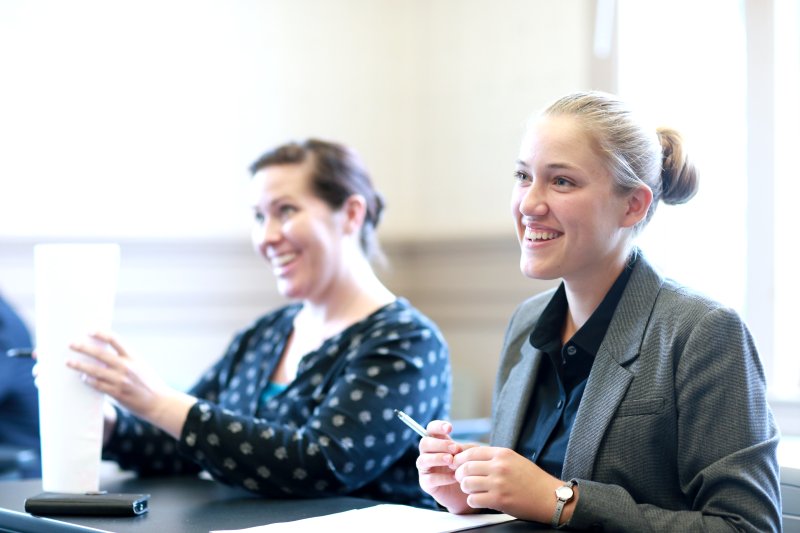 Two female students are sitting at a desk, dressed in business attire.