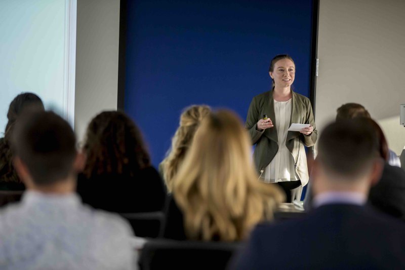 Woman presents in front of a crowded room