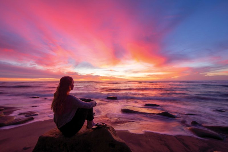 Woman sits on the beach during sunset