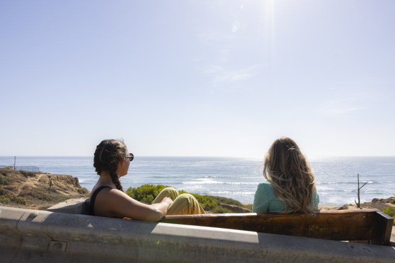 Two students sitting on a bench overlooking the ocean. 