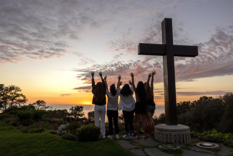 Students raise their hands next to the PLNU cross