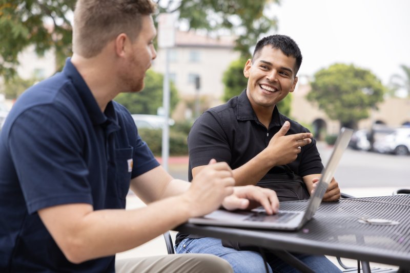 Two PLNU students work on laptops outside