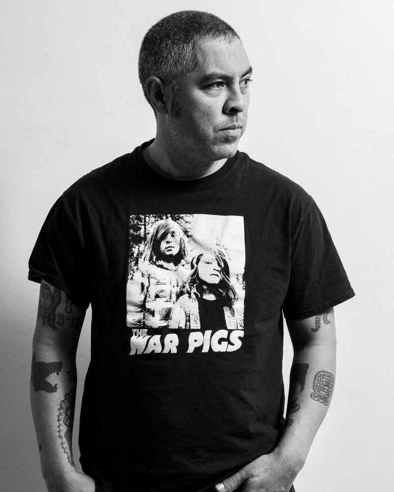 Black and white image of Jason De León wearing a graphic t-shirt and staring to the right