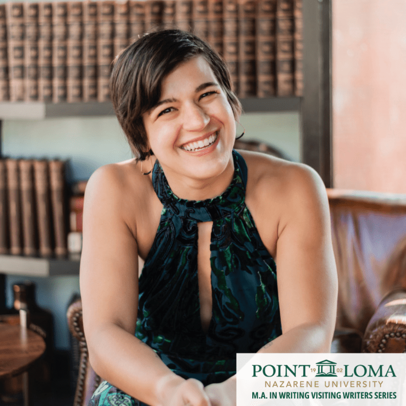 Headshot of Anna Gazmarian seated, smiling at the camera with a blue and green dress on and rows of books behind her.