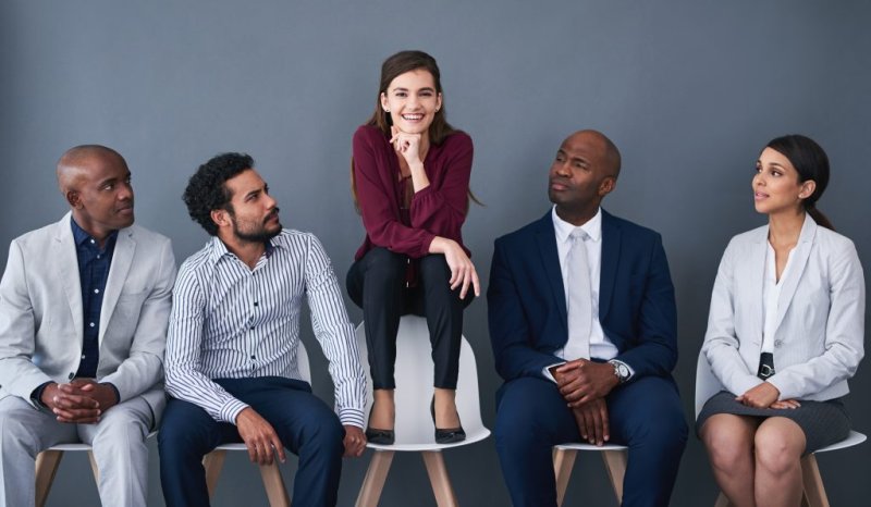 A liberal arts degree student sits on a chair above a group of other business professionals