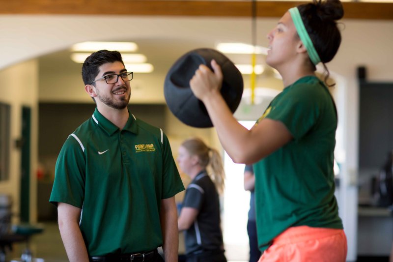 athletic trainer coaching an athlete who is holding a round weight 