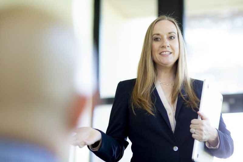 woman holding a laptop speaking to a peer who is near the camera 