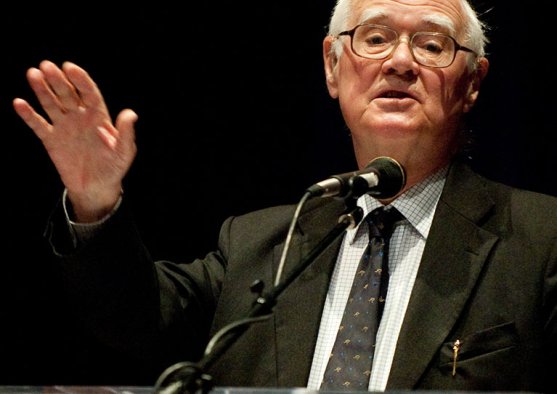 Polkinghorne, an older man, speaks from a podium to community in Crill Hall at PLNU