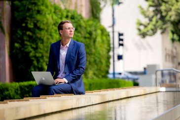 student sitting with laptop and gazing into the distance 