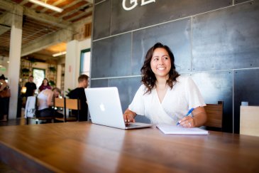 student smiling into the distance as she takes notes for her online class 